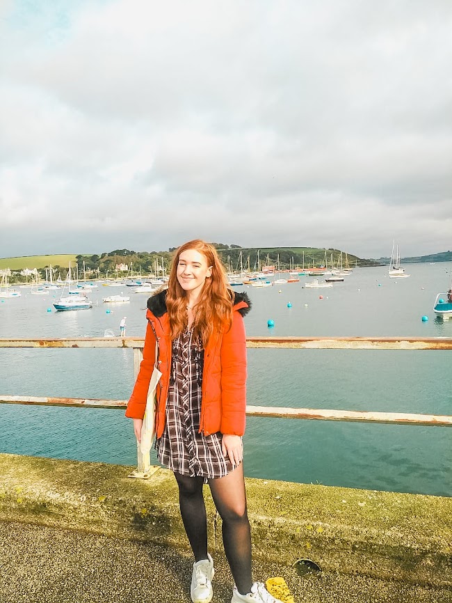 Me at Falmouth Harbour, Cornwall, with boats sitting in the sea behind me.