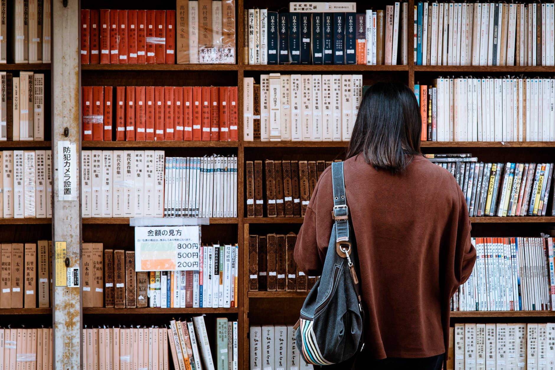 woman wearing brown shirt carrying black leather bag on front of library books
travel as a student